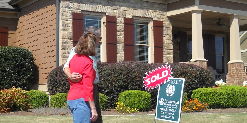 A couple standing in front of a house with a sold sign.