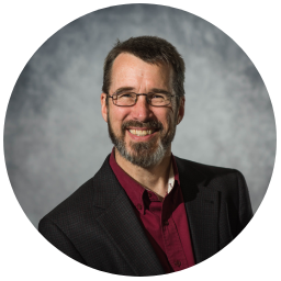 A man with glasses and beard wearing a suit.