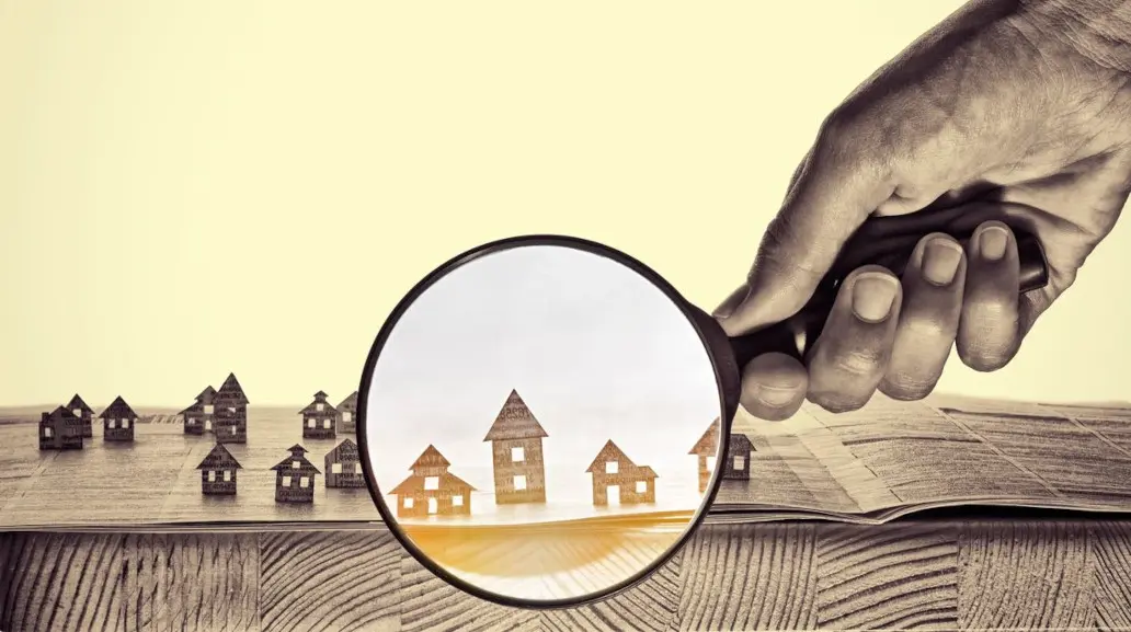 A person holding a magnifying glass over some houses.