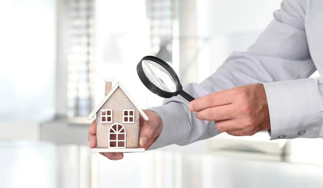 A person holding a magnifying glass over a house.